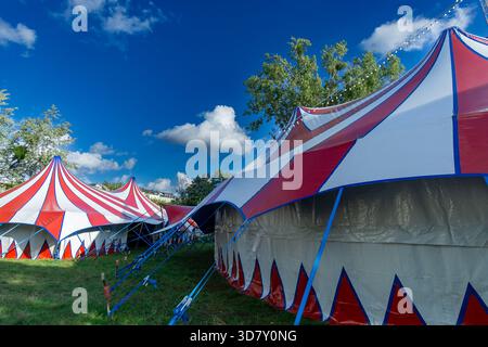 Vista grandangolare delle grandi tende da circo rosse e bianche disposte su un campo erboso vicino a Berlino. Zona fieristica colorata, circo itinerante. Foto Stock