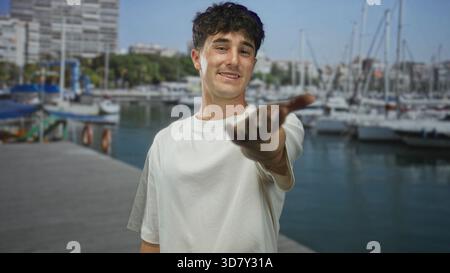 L'uomo raggiunge la mano verso la macchina fotografica presso il molo di un porto accanto alle barche ormeggiate, il braccio allungato e il palmo aperto chiaramente visibili; caldo invito. Foto Stock