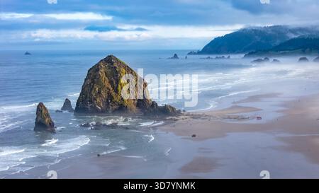 Ripresa aerea sopra Cannon Beach, Oregon, in una mattinata nebbiosa, con Haystack Rock e un paesaggio costiero mostruoso Foto Stock