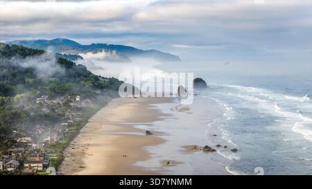 Ripresa aerea sopra Cannon Beach, Oregon, in una mattinata nebbiosa, con Haystack Rock e un paesaggio costiero mostruoso Foto Stock