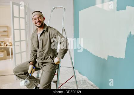 Ritratto di Young Man sorridente mentre dipingeva il muro durante la ristrutturazione Foto Stock