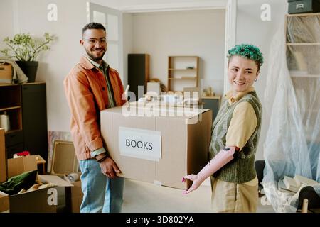 Giovane coppia multietnica che trasporta la scatola durante il trasferimento e la ristrutturazione dell'appartamento Foto Stock