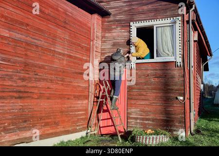L'installazione dell'unità di sorveglianza come tecnico lavora con una donna di mezza età per completare il cablaggio sulla facciata della casa durante il processo di giunzione. Foto Stock