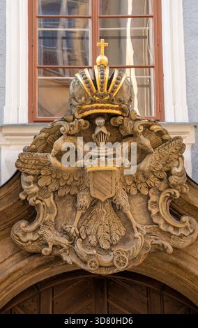 Cresta in pietra dettagliata con una corona, uno scudo e una doppia aquila appollaiata sopra una porta di legno. Ricca scultura araldica che cattura l'eredità reale su un HIS Foto Stock