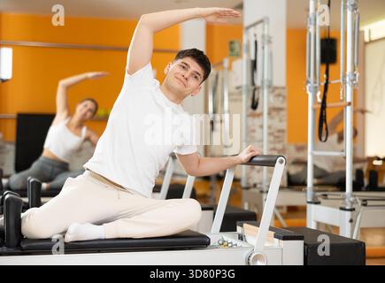 Tizio che fa la curva laterale con il braccio esteso sul riformatore Pilates Foto Stock
