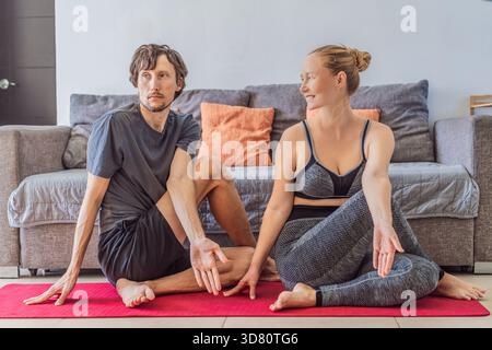 Uomo e donna che praticano yoga insieme in un accogliente salotto, concentrandosi sull'equilibrio, lo stretching e il movimento consapevole. Stile di vita sano, benessere e.. Foto Stock