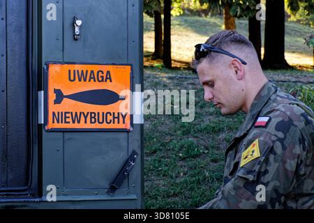 Soldato polacco accanto a un cartello di avvertimento per ordigni inesplosi, con una bomba stilizzata. Foto Stock