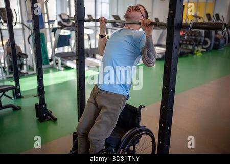L'uomo motivato in sedia a rotelle tira in verticale per rafforzare le braccia e la schiena. Adattamento inclusivo Foto Stock