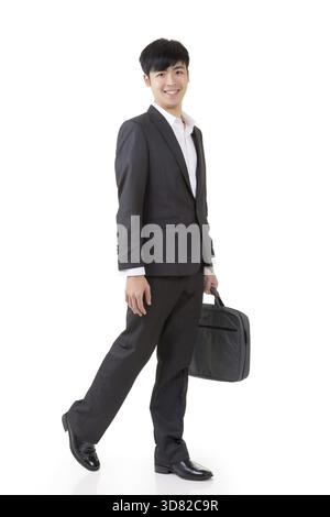 L'uomo d'affari asiatico tiene in mano la valigetta e cammina, ritratto a figura intera isolato su sfondo bianco Foto Stock