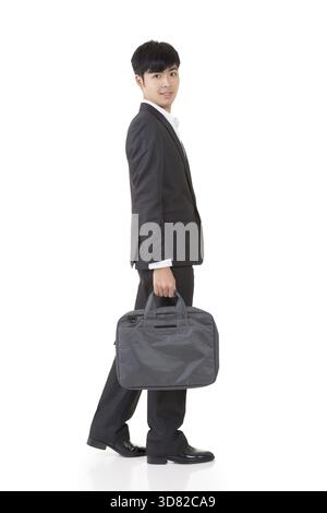 L'uomo d'affari asiatico tiene in mano la valigetta e cammina, ritratto a figura intera isolato su sfondo bianco Foto Stock