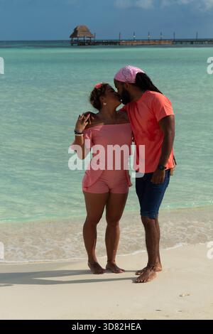 Coppie interrazziali che si baciano su una spiaggia tropicale di sabbia bianca Foto Stock