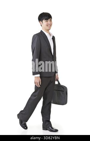 Un giovane uomo d'affari tiene in mano la valigetta e cammina, ritratto a figura intera isolato su sfondo bianco Foto Stock