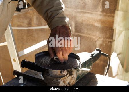 Le mani anziane finalizzano l'utensile di rettifica, le mani intemprate regolano con cura le parti della macchina di rettifica Foto Stock