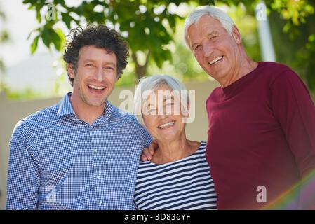 Ritratto, genitori anziani e figlio nel cortile con sorriso, connessione o legame durante le vacanze estive. Bokeh, anziani o famiglie felici all'aperto con Foto Stock