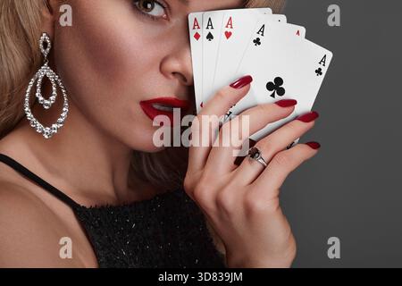 Donna bionda in abito nero lucido e costosi gioielli con diamanti è il vincitore del denaro di Omaha Holdem. Sta sorridendo, mostrando le carte degli assi al Foto Stock