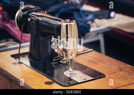 Vista ravvicinata di una macchina da cucire d'epoca su un tavolo in legno, che mette in risalto l'artigianato, gli utensili sartoriali e la riparazione tessile artigianale in un autentico c Foto Stock