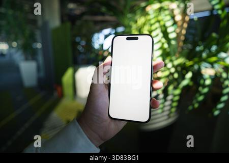 Sfondo dell'ufficio con schermata vuota per il mockup dell'app mobile. Primo piano di uno smartphone con impugnatura maschile con display vuoto, perfetto per la presentazione di design UI/UX, app Foto Stock