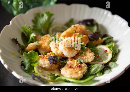Guance croccanti di merluzzo panko servite su freschi green gourmet con limone e grani di pepe rosa - un piatto di pesce di prima qualità per menu raffinati e culinari Foto Stock