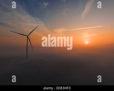 Turbine eoliche che si innalzano al di sopra di un paesaggio nebbioso all'alba con una luce calda Foto Stock