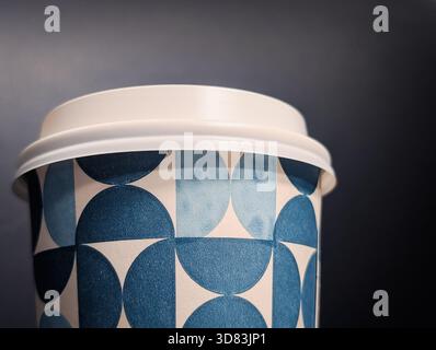 Primo piano estremo di una tazza da caffè usa e getta con motivo geometrico blu e coperchio bianco Foto Stock