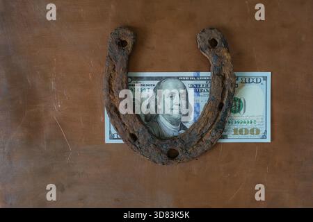Rusty Horseshoe e una legge da cento dollari degli Stati Uniti su sfondo Copper Metal. Paese della fortuna. Simbolo di buona fortuna. Vista dall'alto. Foto Stock