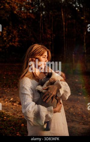 Donna in abito a uncinetto bohémien che tiene il bambino alla luce della foresta autunnale Foto Stock