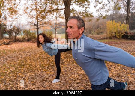 Uomo e donna senior si concentrano sull'equilibrio durante l'esercizio mattutino nel parco Foto Stock