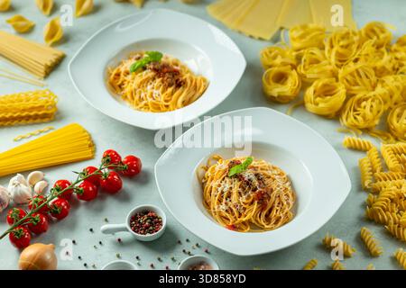 Due porzioni di spaghetti bolognesi circondati da vari formati di pasta cruda e verdure fresche Foto Stock