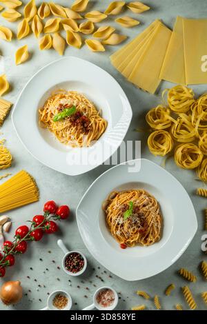 Gli spaghetti bolognesi si stanno gustando un pasto circondato da vari tipi di pasta cruda e componenti di cottura freschi Foto Stock