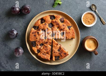 Torta di prugne autunnale calda su un piatto con sfondo in pietra blu. Vista dall'alto, disposizione piatta. Foto Stock