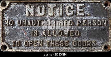 Primo piano di un cartello in metallo pressofuso con testo in rilievo che avverte che non è consentito aprire queste porte a persone non autorizzate Foto Stock