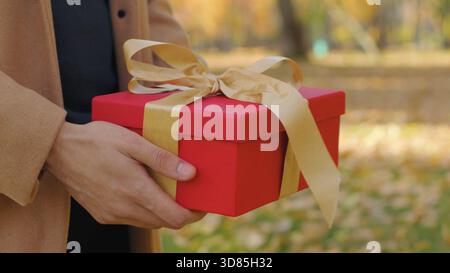 Coppia ravvicinata irriconoscibile con confezione regalo in città uomo sconosciuto fidanzato congratularsi donna fidanzata che regala regalo con nastro d'oro anniversario Foto Stock