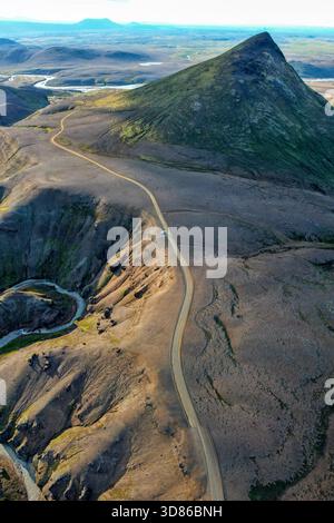 Vista aerea della strada tortuosa che serpeggia attraverso il paesaggio vulcanico e aspro verso le maestose montagne di Kerlingarfjöll, un arazzo di verdi e. Foto Stock