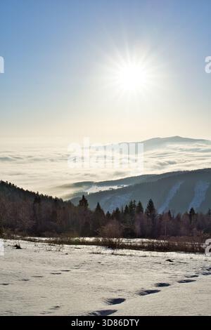 Vista aerea del sole che splende sulle montagne innevate e un mare di nebbia, dipingendo il paesaggio in tonalità di bianco e blu, Spisska nova VES, Kosic Foto Stock