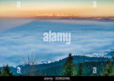 Vista aerea della maestosa montagna che getta una lunga ombra su un mare di nuvole, con la foresta sottostante che aggiunge un tocco di verde, Spisska nova VES, Kosi Foto Stock
