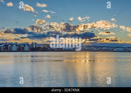 Paesaggio urbano lungo il lungomare al tramonto con spettacolari nuvole, sfondo di montagna e riflessi dorati. Foto Stock