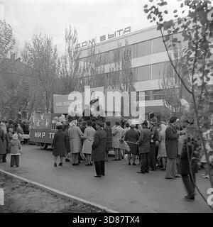 Slavyansk, Ucraina, URSS - 1970s: Una sfilata di manifestazioni festive in via Karl Marx (ora via Tsentralna). Le colonne dei residenti marciano oltre l'edificio modernista "Dom Byta" (House of Life Services). I partecipanti portano bandiere, palloncini, striscioni con slogan come "abbiamo bisogno di pace!" e ritratti di leader sovietici, tra cui Leonid Brezhnev. La gente è vestita con cappotti autunnali. Questa foto d'archivio in bianco e nero cattura i rituali ideologici, la moda e l'atmosfera sociale della tranquilla città industriale di Donbas. Foto Stock