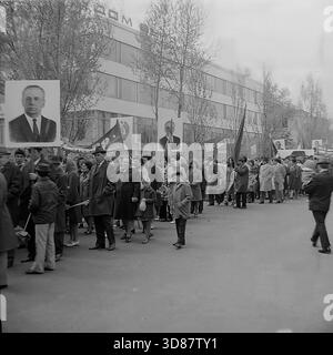 Slavyansk, Ucraina, URSS - 1970s: Una sfilata di manifestazioni festive in via Karl Marx (ora via Tsentralna). Le colonne dei residenti marciano oltre l'edificio modernista "Dom Byta" (House of Life Services). I partecipanti portano bandiere, palloncini, striscioni con slogan come "abbiamo bisogno di pace!" e ritratti di leader sovietici, tra cui Leonid Brezhnev. La gente è vestita con cappotti autunnali. Questa foto d'archivio in bianco e nero cattura i rituali ideologici, la moda e l'atmosfera sociale della tranquilla città industriale di Donbas. Foto Stock