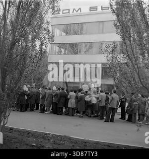 Slavyansk, Ucraina, URSS - 1970s: Una sfilata di manifestazioni festive in via Karl Marx (ora via Tsentralna). Le colonne dei residenti marciano oltre l'edificio modernista "Dom Byta" (House of Life Services). I partecipanti portano bandiere, palloncini, striscioni con slogan come "abbiamo bisogno di pace!" e ritratti di leader sovietici, tra cui Leonid Brezhnev. La gente è vestita con cappotti autunnali. Questa foto d'archivio in bianco e nero cattura i rituali ideologici, la moda e l'atmosfera sociale della tranquilla città industriale di Donbas. Foto Stock