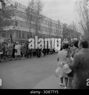 Slavyansk, Ucraina, URSS - 1970s: Una sfilata di manifestazioni festive in via Karl Marx (ora via Tsentralna). Le colonne dei residenti marciano oltre l'edificio modernista "Dom Byta" (House of Life Services). I partecipanti portano bandiere, palloncini, striscioni con slogan come "abbiamo bisogno di pace!" e ritratti di leader sovietici, tra cui Leonid Brezhnev. La gente è vestita con cappotti autunnali. Questa foto d'archivio in bianco e nero cattura i rituali ideologici, la moda e l'atmosfera sociale della tranquilla città industriale di Donbas. Foto Stock