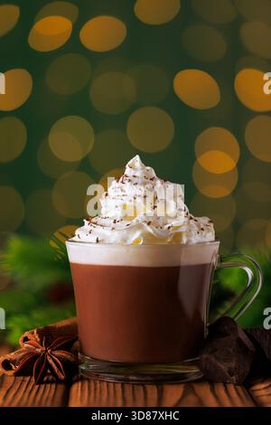Cioccolata calda con panna montata in tazza di vetro su sfondo verde di luci bokeh scintillanti della ghirlanda Foto Stock