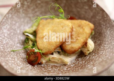 Questa immagine mostra due filetti di pesce impanati croccanti disposti su un'elegante ciotola, accompagnati da un mix di verdure fresche. La presentazione Highlig Foto Stock