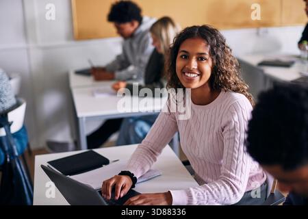 Ritratto ad alto angolo di una studentessa sorridente che siede con un computer portatile alla scrivania in classe a scuola Foto Stock