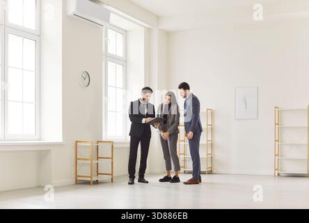 Agente immobiliare, coppia di clienti, uomini d'affari in piedi, che guardano un tablet, discutono dei piani d'ufficio Foto Stock