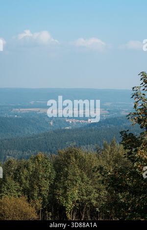 Ampio paesaggio di colline e vallate densamente boscose, con un piccolo borgo tradizionale visibile in lontananza Foto Stock