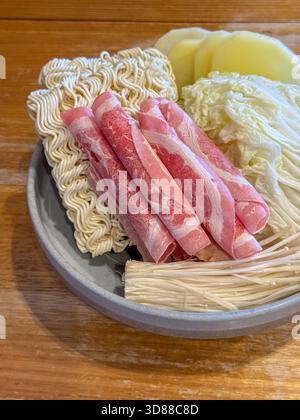 Gli ingredienti per un pasto caldo vengono presentati ordinatamente su un piatto, con carne a fette, spaghetti e verdure varie. Foto Stock