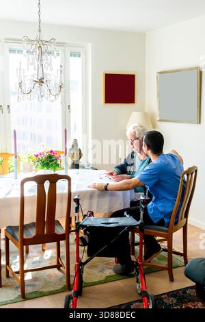 Assistente infermieristico maschile seduto con una donna anziana che prende medicine a casa Foto Stock