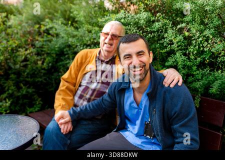 Ritratto di un caregiver maschio felice che trascorre il tempo libero con un uomo anziano nel parco Foto Stock