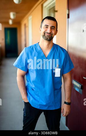 Ritratto di sicuro operatore sanitario maschile che indossa scrub medici in piedi con mano in tasca Foto Stock