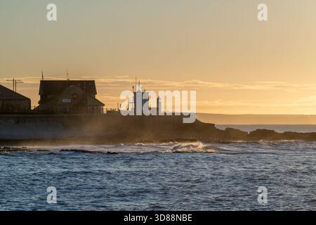 La luce mattutina sulla guardia costiera di Porthcawl e sulla stazione dei battelli di salvataggio mentre le onde si infrangono lungo la costa in un'alba autunnale nel Galles meridionale Foto Stock